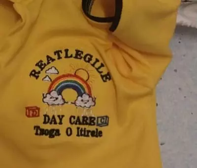 Reatlegile Day Care logo embroidered on a yellow uniform shirt